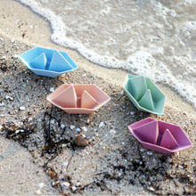 Load image into Gallery viewer, Four colourful silicone boats on a sandy beach with waves in the background