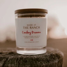Load image into Gallery viewer, Candle labeled &#39;Made at the Ranch Cowboy Dreams&#39; on a wooden surface with a blurred background