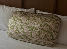 Load image into Gallery viewer, Floral-patterned pillow cover on a bed with white pillows and a brown headboard.