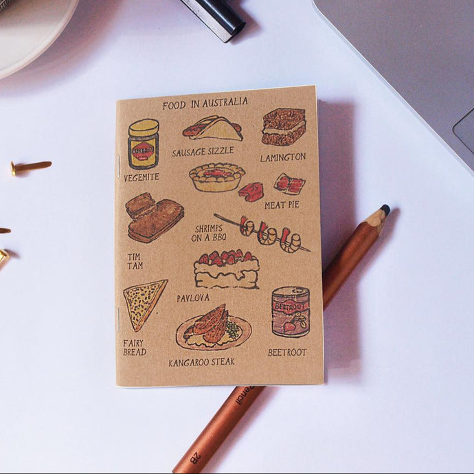 Notebook with illustrations of Australian food on a desk with stationery items.