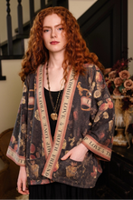 Load image into Gallery viewer, A woman with long curly red hair models a dark brown open-front kimono jacket featuring a vintage wine bottle and floral pattern, with beige trim printed with 'LOVE &amp; TRUTH' text. She is standing in a dimly lit interior with a staircase in the background.