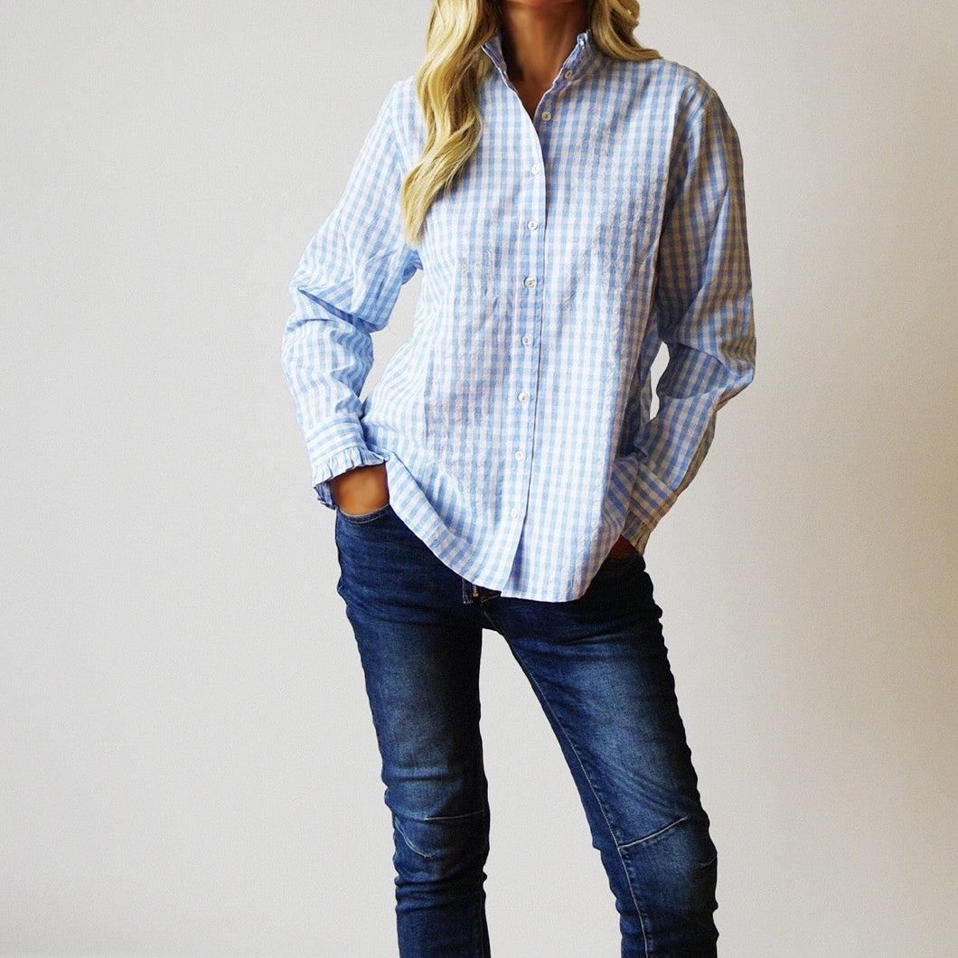 Person wearing a blue and white checkered shirt and dark jeans against a plain background
