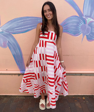 Load image into Gallery viewer, Woman in a red and white patterned dress standing in front of a colorful mural.