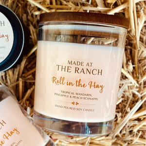 Large candle labeled 'Made at the Ranch Roll in the Hay' on a bed of straw.