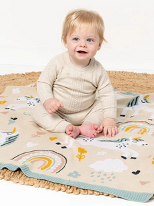 Baby sitting on a colorful blanket with unicorn design on a white background