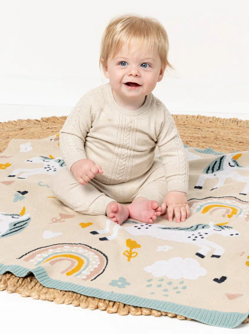 Baby sitting on a colorful blanket with unicorn design on a white background