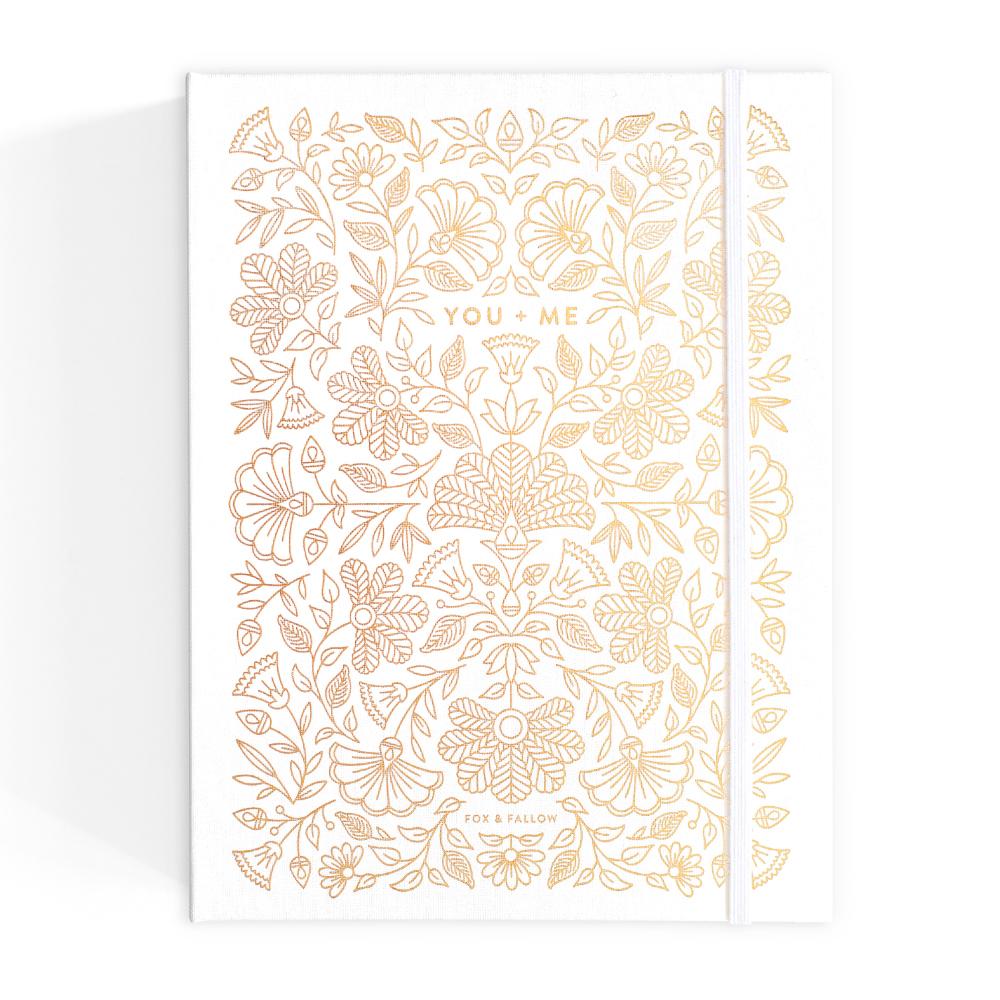 Gold floral patterned wedding journal with 'You + Me' text on a white background