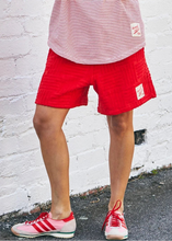 Load image into Gallery viewer, Person wearing a pink 'LOVE' tank top and red shorts standing against a white brick wall.